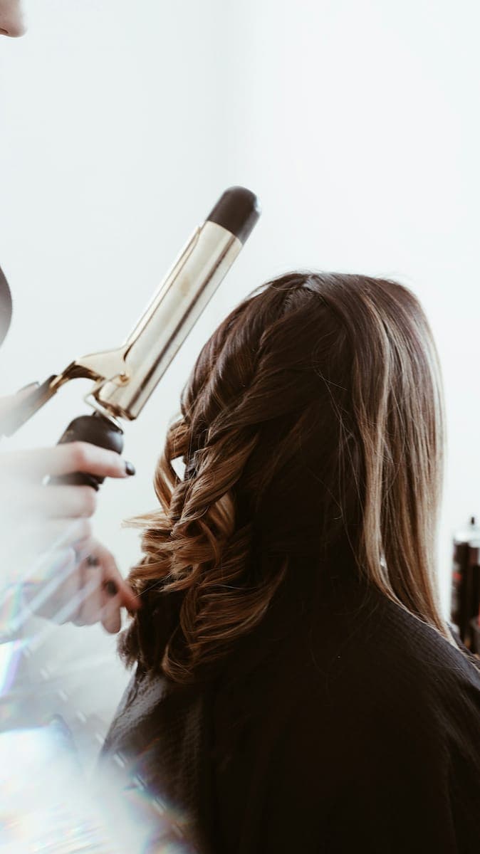 Une coiffeuse réalise des boucles dans les cheveux de sa cliente.